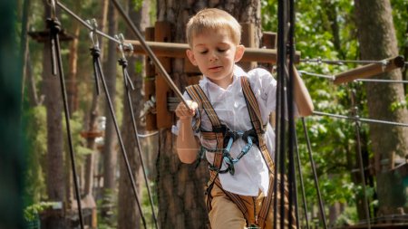 Foto de Retrato de niño lindo sosteniendo la cuerda de seguridad en el parque de aventura extrema al aire libre. Infancia activa, estilo de vida saludable, niños jugando al aire libre, niños en la naturaleza - Imagen libre de derechos