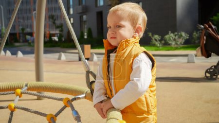 Téléchargez les photos : Un petit garçon qui pleure, debout sur la cour de récréation à swing. Enfants jouant en plein air, enfants dehors, vacances d'été et vacances - en image libre de droit