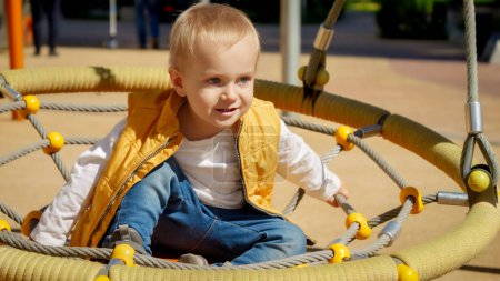 Foto de Un niño balanceándose en el patio del parque. Niños jugando al aire libre, niños afuera, vacaciones de verano y vacaciones - Imagen libre de derechos