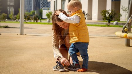 Photo for Little toddler boy holding mother while she is putting on him shoes on the playground. - Royalty Free Image