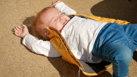 Téléchargez les photos : Bébé garçon très contrarié pleurant et tombant par terre dans la rue. Enfants bouleversés, émotions négatives, problèmes d'enfants - en image libre de droit
