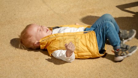 Téléchargez les photos : Pleurer et crier petit garçon couché sur le sol dans la rue. Enfants bouleversés, émotions négatives, problèmes d'enfants - en image libre de droit