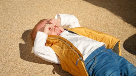 Photo for Portrait of crying and screaming toddler boy lying on ground and rubbing eyes with tears. - Royalty Free Image