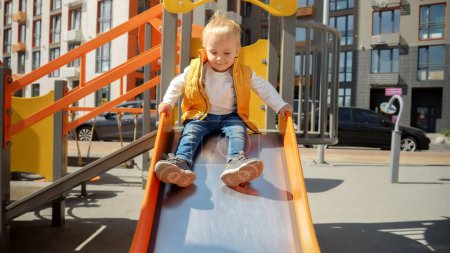 Photo for Cute baby boy sitting on the top of slide and riding down. Happy parenting, family having time together, kids and parents outdoors - Royalty Free Image