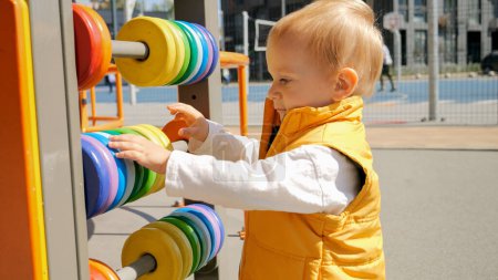 Téléchargez les photos : Portrait de petit garçon jouant avec un boulier coloré à l'aire de jeux. Développement des enfants, éducation des enfants, apprentissage des bébés - en image libre de droit
