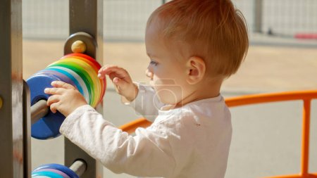 Photo for Portrait of little boy spinning colorful circles on abacus at playground. Children developments, kids education, baby learning - Royalty Free Image