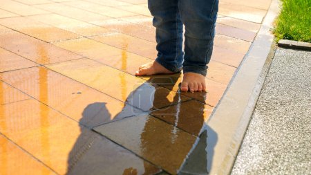 Photo for Closeup of barefoot baby walking over puddle and splashing water. Kids outdoors, children in nature, baby playing outside - Royalty Free Image