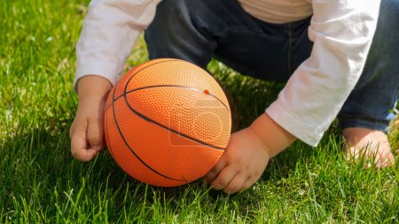 Foto de Primer plano del niño descalzo jugando con la pelota en el césped de hierba verde. Niños al aire libre, niños en la naturaleza, bebé jugando al aire libre - Imagen libre de derechos