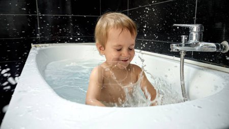 Téléchargez les photos : Petit garçon jouissant de son temps de bain et jouant avec l'eau, la mousse et l'éponge. L'image met en évidence l'importance de l'heure du bain comme partie essentielle de la routine d'hygiène d'un bébé. - en image libre de droit