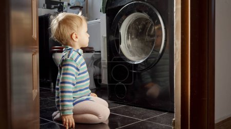Foto de Niño buscando con interés en el tambor giratorio de la lavadora. Hacer tareas domésticas y tareas, educación y desarrollo de los niños - Imagen libre de derechos