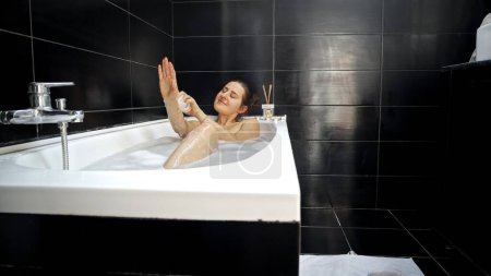 Téléchargez les photos : Femme prenant bain dans la salle de bain avec des murs noirs. Hygiène féminine, détente dans la salle de bain, beauté et santé - en image libre de droit