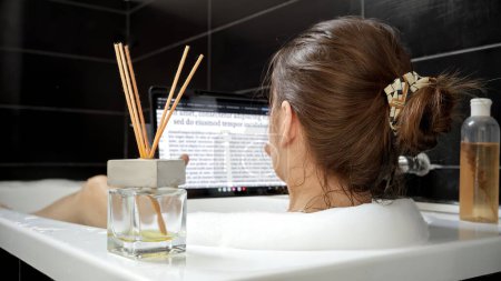 Téléchargez les photos : Une femme prend un bain relaxant et surfe sur le Web sur sa tablette - en image libre de droit