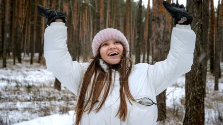 Foto de Retrato de una adolescente feliz y sonriente atrapando y riendo de nieve cayendo en el bosque. Gente jugando al aire libre, vacaciones de invierno y vacaciones, ocio activo - Imagen libre de derechos
