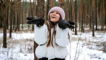 Photo for Smiling teenage girl catching snowflakes in forest covered with snow at winter. People playing outdoors, winter holidays and vacation, active leisure - Royalty Free Image