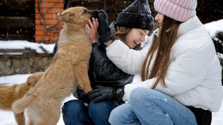Foto de Dos chicas con perros jugando en la nieve durante las nevadas. Niños con animales, juegos con mascotas - Imagen libre de derechos
