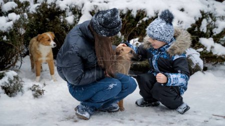 Foto de Niño con hermana jugando con perros en la nieve en el patio trasero de la casa. Niños con animales, juegos con mascotas - Imagen libre de derechos
