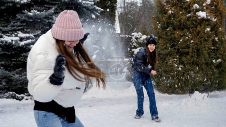 Foto de Dos niñas adolescentes riendo felices jugando bolas de nieve en el patio trasero en el día de invierno nevado. Gente jugando al aire libre, vacaciones de invierno y vacaciones, ocio activo - Imagen libre de derechos