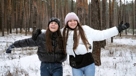 Photo for Two laughing teenage girls cheering and laughing while catching falling snowflakes in winter forest. - Royalty Free Image