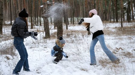Foto de Dos adolescentes jugando con un niño en la nieve y lanzando bolas de nieve. Gente jugando al aire libre, vacaciones de invierno y vacaciones, ocio activo - Imagen libre de derechos