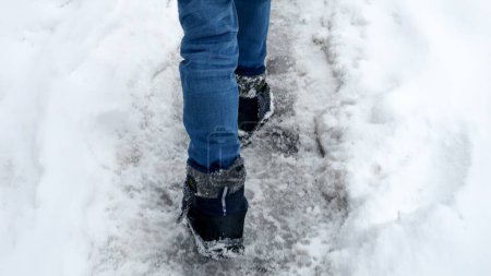 Foto de Primer plano de los pies de los niños en botas de nieve caminando por el camino cubierto de nieve después de la tormenta. - Imagen libre de derechos