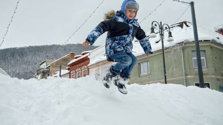 Téléchargez les photos : Joyeux garçon souriant sautant dans une grosse dérive de neige et riant. Bébé gai, enfants jouant à l'hiver, vacances de Noël - en image libre de droit