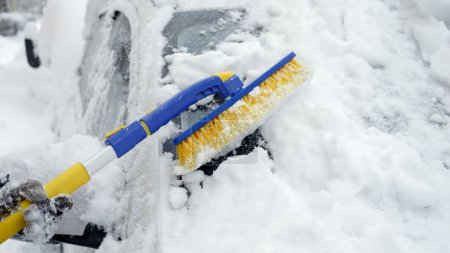 Foto de Primer plano de una mujer usando un cepillo de nieve para limpiar la nieve del parabrisas de su coche. Concepto de clima invernal, mantenimiento del automóvil y preparación para condiciones nevadas - Imagen libre de derechos