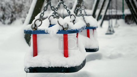 Foto de Copos de nieve cayendo en columpios vacíos en el parque público y cubriendo el parque con nieve. Concepto de vacaciones de invierno, mal tiempo y ventisca. - Imagen libre de derechos
