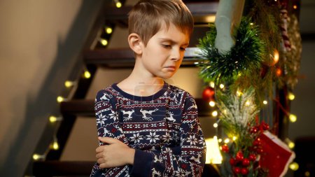 Téléchargez les photos : Portrait de garçon malheureux bouleversé assis seul sur des escaliers en bois en attendant que le Père Noël vienne la nuit de Noël. - en image libre de droit