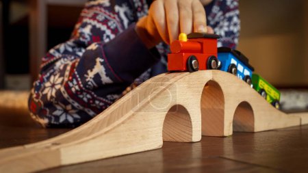 Photo for Closeup of boy in pajamas lying on floor and playing with toy wooden train and railroad - Royalty Free Image