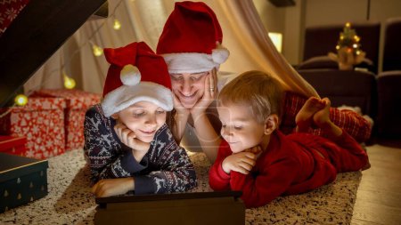 Photo for Portrait of happy cheerful family celebrating Christmas and New Year watching movies on tablet computer. Winter holidays, celebrations and party - Royalty Free Image