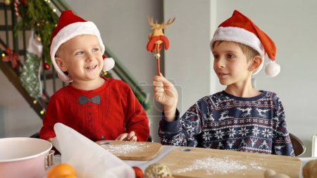 Foto de Dos niños jugando y cantando en una mañana de Navidad mientras están sentados en la cocina. Vacaciones de invierno, celebraciones y fiestas - Imagen libre de derechos