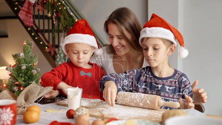 Téléchargez les photos : Mère heureuse aidant leurs fils à cuisiner des biscuits de Noël et des biscuits pour les célébrations. Vacances d'hiver, fêtes et fêtes - en image libre de droit