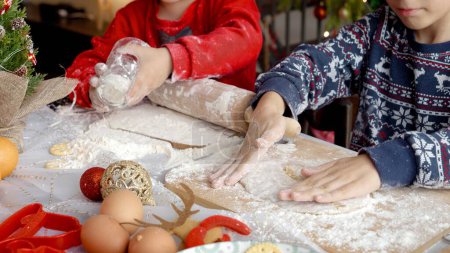 Photo for Closeup of two boys making dough and using rolling pin while making dough for traditional Christmas cookies. Winter holidays, celebrations and party - Royalty Free Image