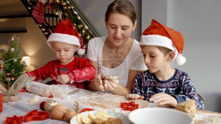 Téléchargez les photos : Bonne famille avec des enfants cuisiner et préparer des biscuits pour le Père Noël le matin de Noël. Vacances d'hiver, fêtes et fêtes - en image libre de droit