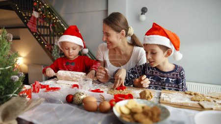 Téléchargez les photos : Joyeux famille faisant de la pâte et des biscuits au four pour le Père Noël sur Noël. Vacances d'hiver, fêtes et fêtes - en image libre de droit
