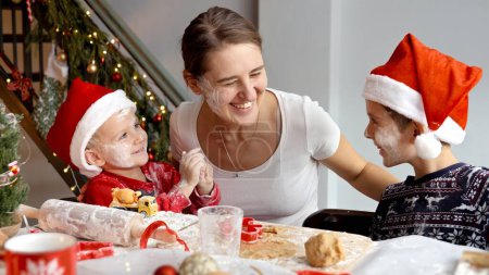 Photo for Happy cheerful family getting messy and dirty in flour and dough while cooking Christmas cookies and biscuits on kitchen. Winter holidays, celebrations and party - Royalty Free Image