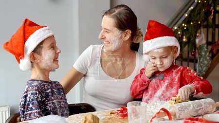 Téléchargez les photos : Joyeux enfants joyeux jouant avec la mère et jetant des fleurs les uns dans les autres tout en faisant des biscuits pour Noël. Vacances d'hiver, fêtes et fêtes. - en image libre de droit