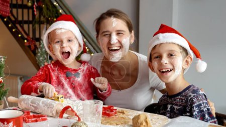 Téléchargez les photos : Portrait de famille heureux riant avec les enfants est devenu salissant tout en cuisinant et en se préparant pour Noël et le Nouvel An sur la cuisine. Vacances d'hiver, fêtes et fêtes - en image libre de droit