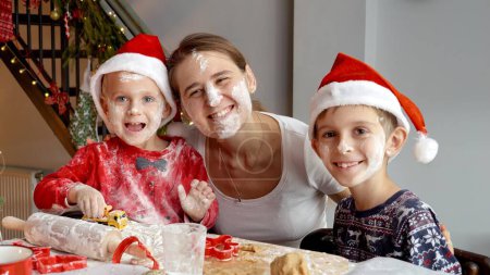 Photo for Portrait of happy funny family in Santa's hats got messy and dirty while preparing and cooking on kitchen for Christmas celebrations. - Royalty Free Image