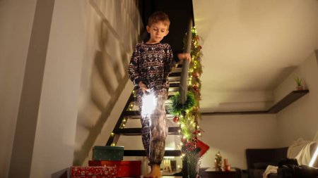 Foto de Feliz niño emocionado con linterna bajando las escaleras en la noche de Navidad y en busca de regalos y regalos de Santa. - Imagen libre de derechos