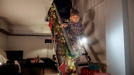 Téléchargez les photos : Petit garçon en pyjama descendant les escaliers avec une torche la nuit de Noël. - en image libre de droit