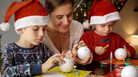 Téléchargez les photos : Jeune mère avec deux enfants se préparant pour Noël et faisant des décorations faites à la main. Vacances d'hiver, temps en famille ensemble, enfants avec les parents célébrant - en image libre de droit