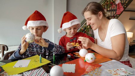 Téléchargez les photos : Enfants avec mère peinture et décoration boules de Noël dans le salon. Vacances d'hiver, temps en famille ensemble, enfants avec les parents célébrant - en image libre de droit