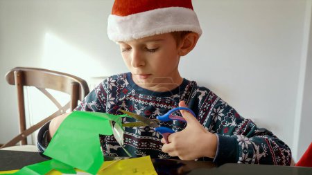 Téléchargez les photos : Portrait de petit garçon découpant des décorations en papier coloré pour Noël ou le Nouvel An - en image libre de droit