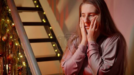 Photo for Young woman got scared and nervous on Christmas night. Police or ambulance car lights illuminating the room. Crime, ambulance, injury, problems with law and theft on winter holidays and celebrations - Royalty Free Image