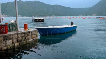 Foto de Barco de pesca de madera con motor amarrado en el muelle de piedra mientras llueve en el mar. - Imagen libre de derechos