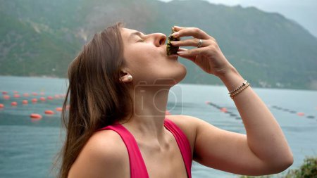 Foto de Retrato de mujer morena disfrutando comiendo ostras crudas en la costa del mar durante la lluvia. - Imagen libre de derechos