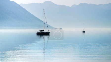 Téléchargez les photos : Silhouette de deux yachts amarrés dans un port de mer calme avec brume matinale montante et brouillard. - en image libre de droit