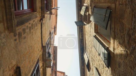 Photo for View from the ground on old narrow street with stone buildings and tiled roofs at old European city. - Royalty Free Image