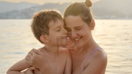 Photo for Portrait of loving mother and son hugging each other while relaxing on the sea against sunset light rays. - Royalty Free Image
